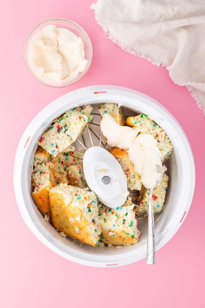 Crumbled funfetti cake with frosting added in a mixing bowl