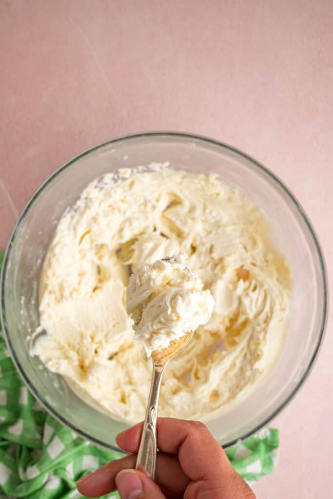 spoon holding a scoop of buttercream filling above the mixing bow