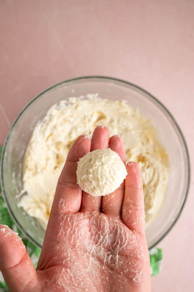 hand holding a rolled ball of buttercream filling above a glass mixing bowl