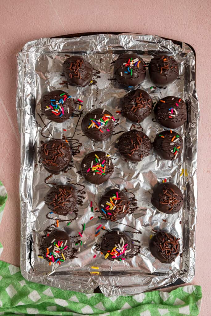 chocolate coated buttercream truffles with sprinkles on a foil lined baking sheet