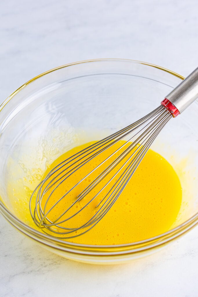 egg yolks being whisked in a glass bowl to prepare creme brulee custard
