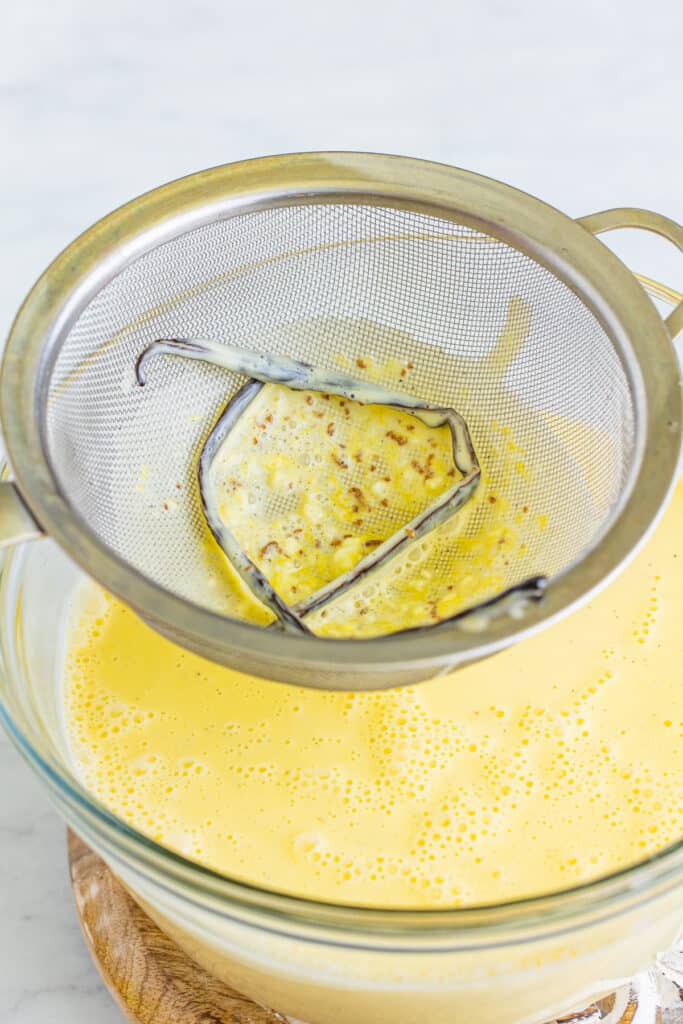 creme brulee custard being strained through a fine mesh strainer into a bowl