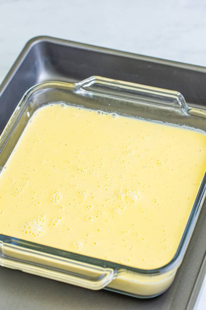 creme brulee custard poured into a glass baking dish set inside a roasting pan