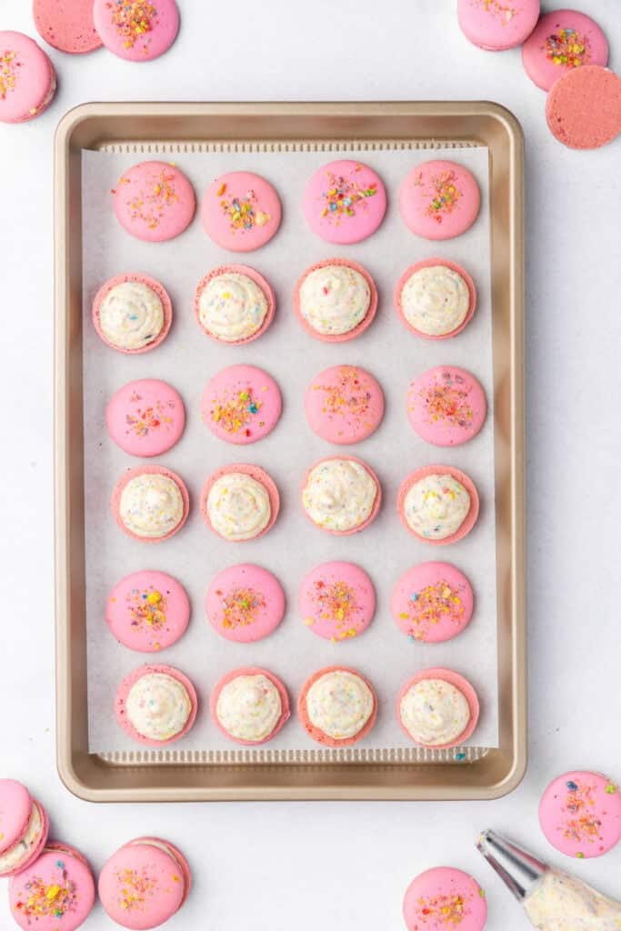 macaron shells filled with fruity pebbles buttercream on a baking sheet