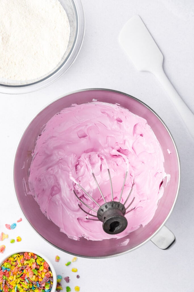 Pink colored meringue in a stand mixer bowl after adding gel food coloring