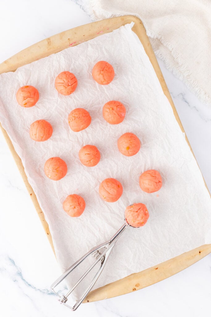 Pink truffle dough scooped into uniform balls and arranged on parchment paper using a cookie scoop.