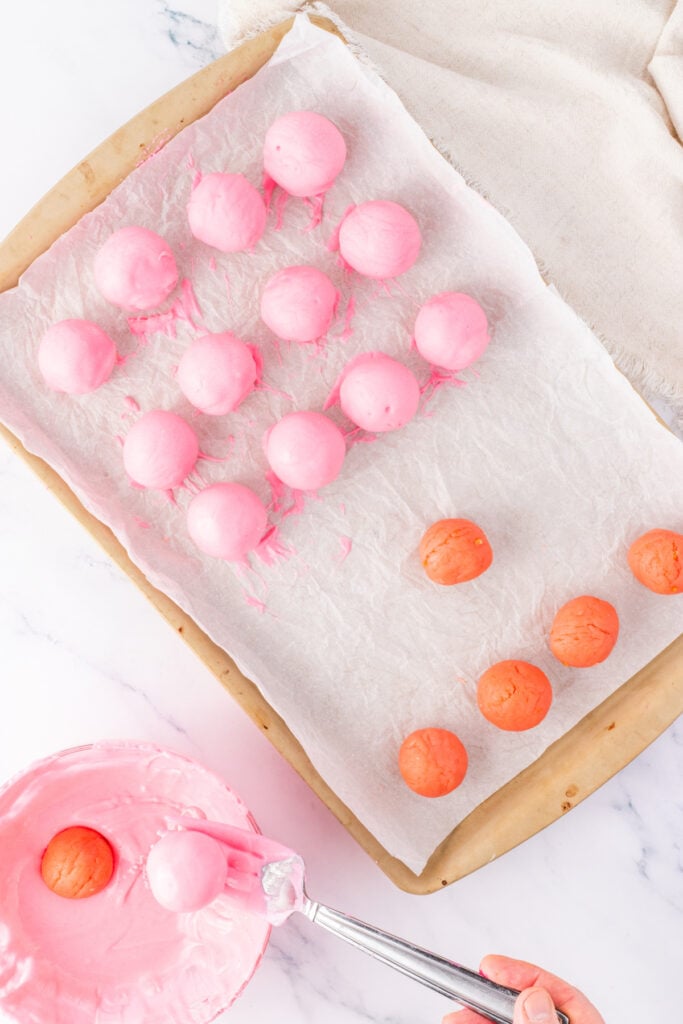 Pink truffle balls arranged on parchment paper with some freshly dipped in pink coating and others waiting to be coated.