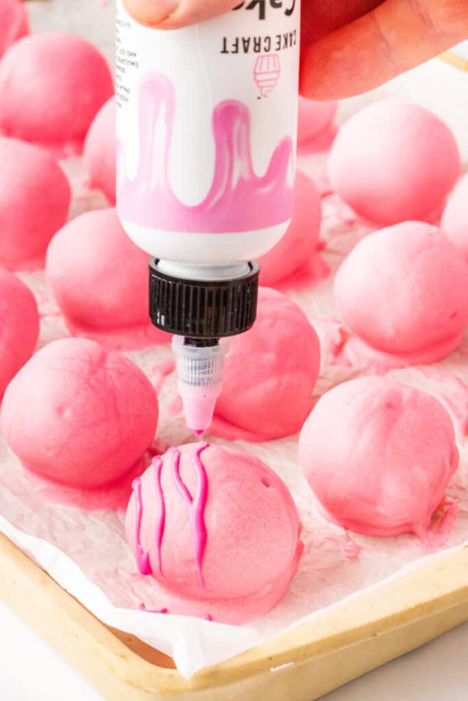 Pink Valentine truffles being drizzled with pink candy coating while resting on parchment paper.