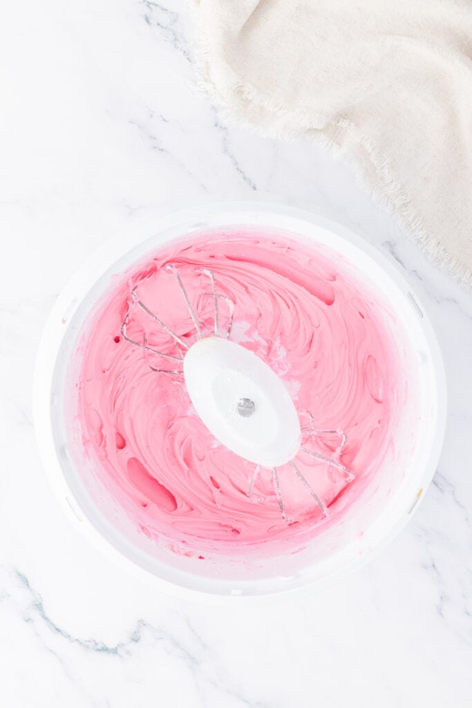 Pink frosting being whipped in a mixing bowl until smooth and fluffy for coating the truffles.