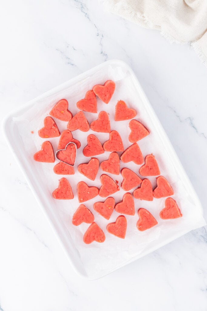 Heart-shaped strawberry cake truffles cut and arranged on a parchment-lined tray before dipping