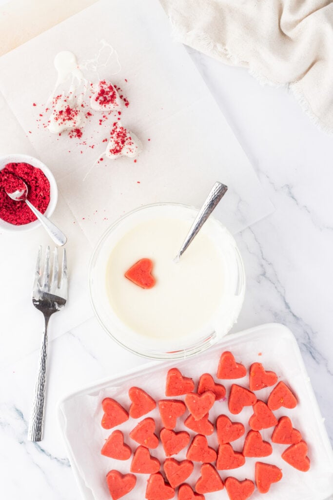 Strawberry cake hearts being dipped into melted vanilla candy coating
