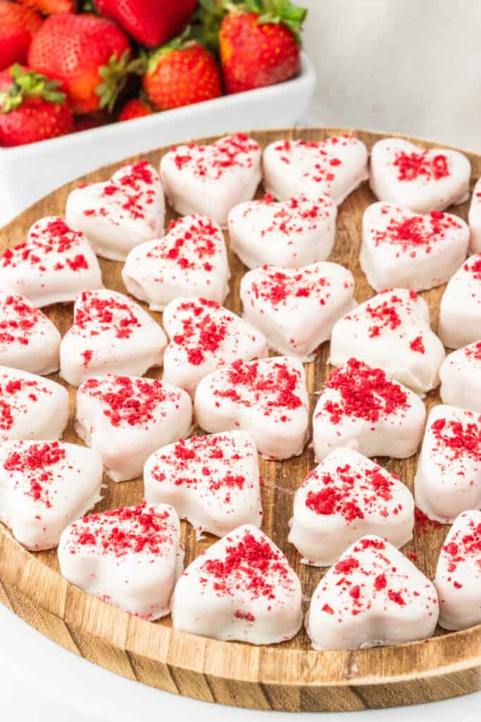 Strawberries and cream truffle hearts arranged on a wooden board with fresh strawberries in the background