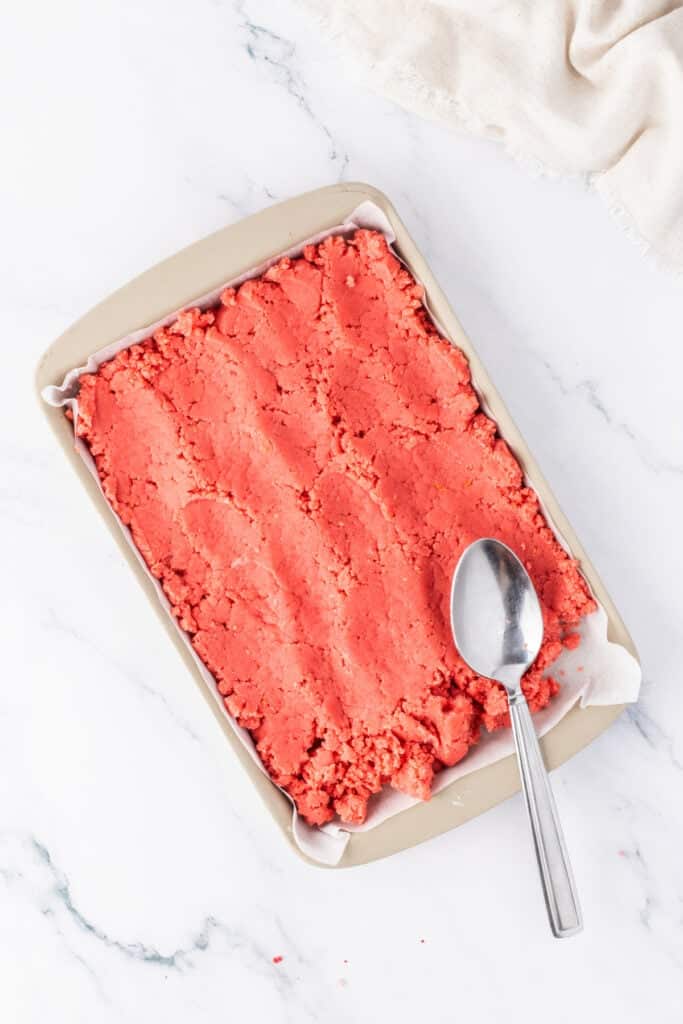Strawberry cake mixture pressed into a baking pan before cutting into shapes