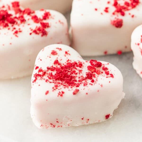 Close-up of a single strawberries and cream truffle heart coated in white candy and topped with crushed freeze-dried strawberries
