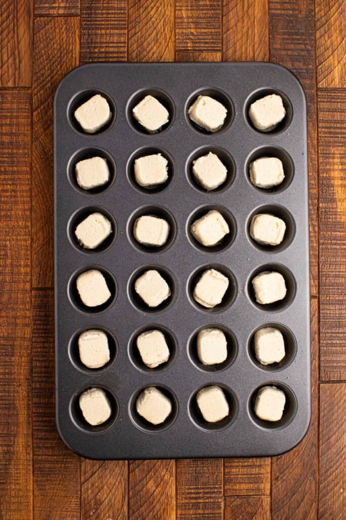 Mini muffin pan filled with unbaked sugar cookie dough pieces ready to be baked into cookie cups