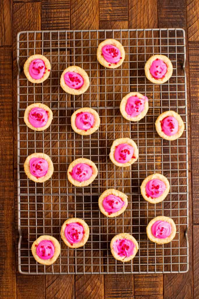 Valentine sugar cookie cups cooling on a wire rack with pink frosting and red heart sprinkles