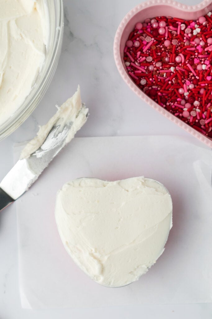 Heart shaped cake fully coated with a smooth layer of white frosting on a cutting board