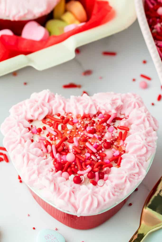 Heart shaped cake decorated with piped pink frosting around the edges and Valentine sprinkles in the center
