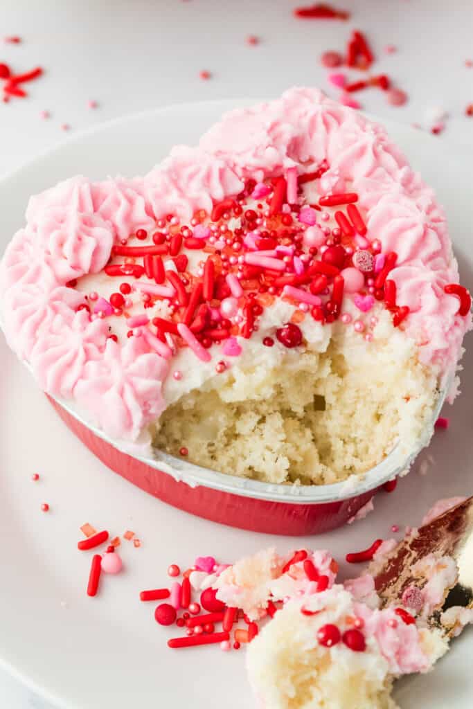 Heart shaped Valentine lunch box cake with a bite removed, showing soft vanilla cake crumb and pink frosting