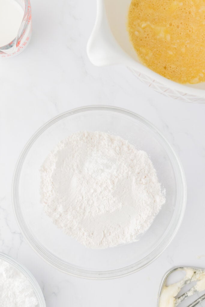 Dry cake ingredients measured in a glass bowl on a white marble surface