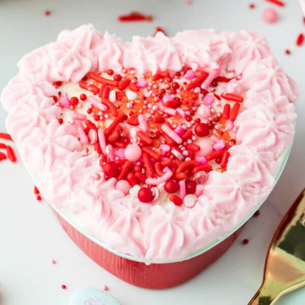 square-cropped image of a heart-shaped Valentine lunch box cake with pink frosting and red sprinkles