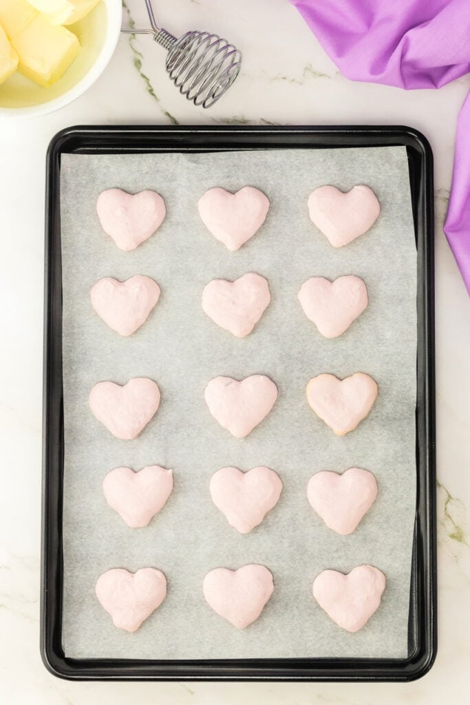 heart shaped pink macaron shells resting on parchment paper on a baking sheet after baking