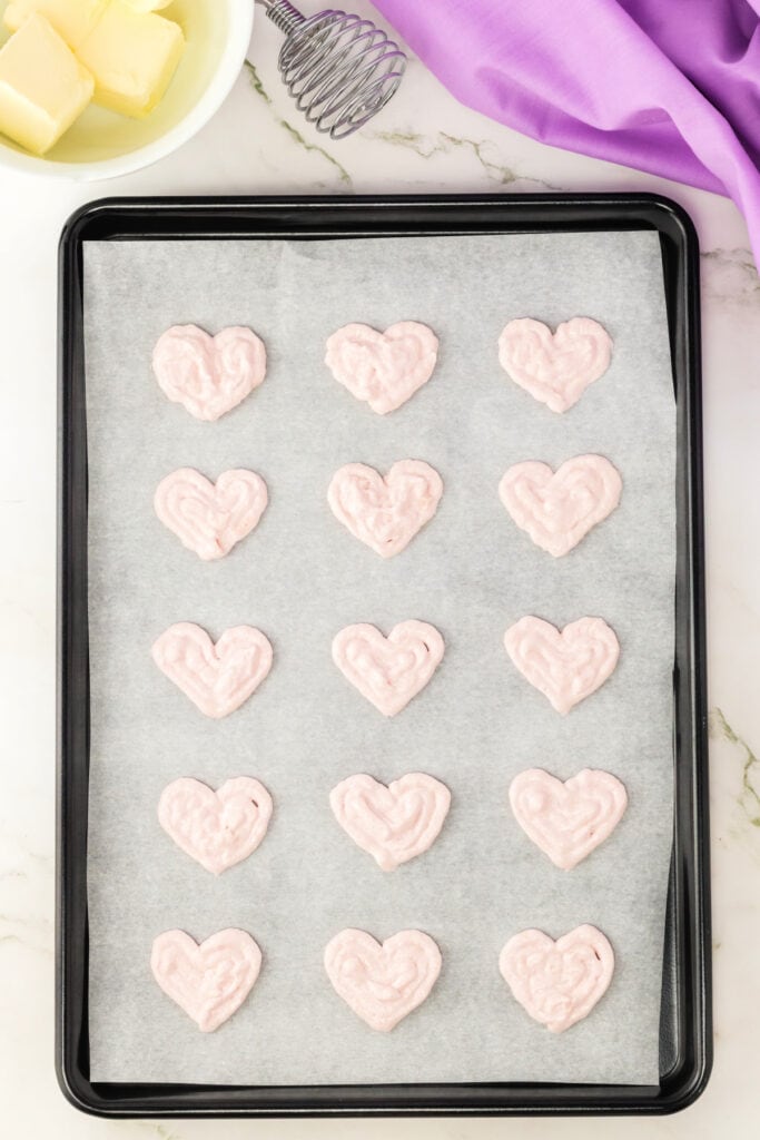 heart shaped macaron shells resting on parchment paper before baking