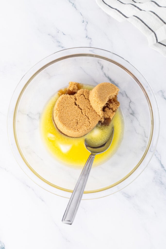 Brown sugar and melted butter in a glass mixing bowl with spoon