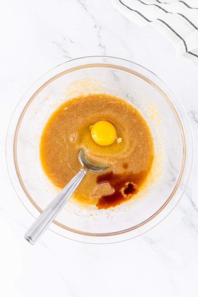 Egg and vanilla added to blondie batter in a glass bowl