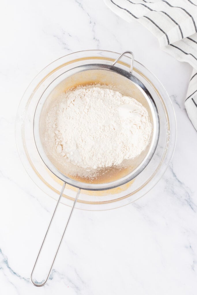 Dry ingredients being sifted into blondie batter using a fine mesh strainer