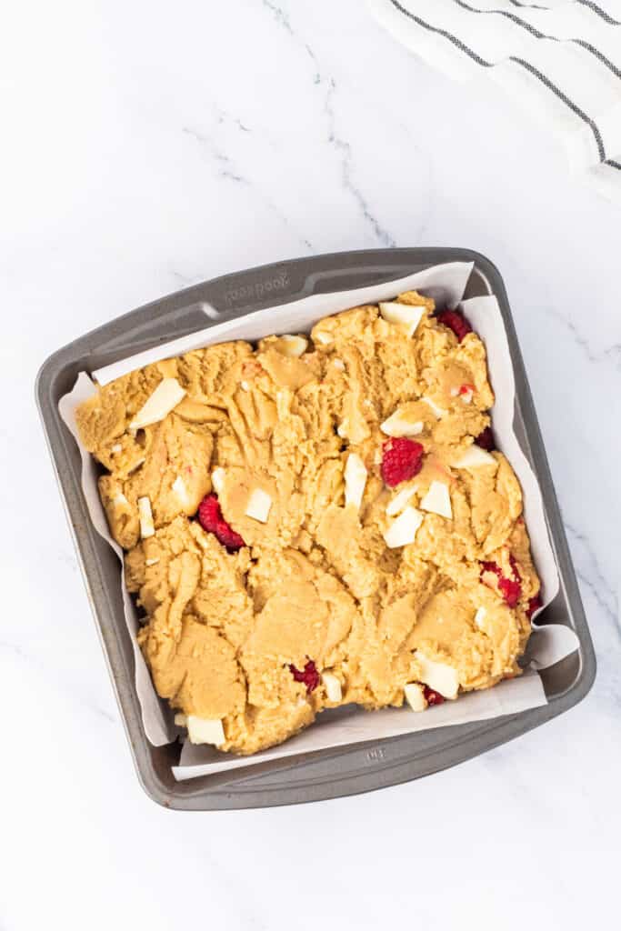 White chocolate raspberry blondie batter spread into a parchment-lined baking pan
