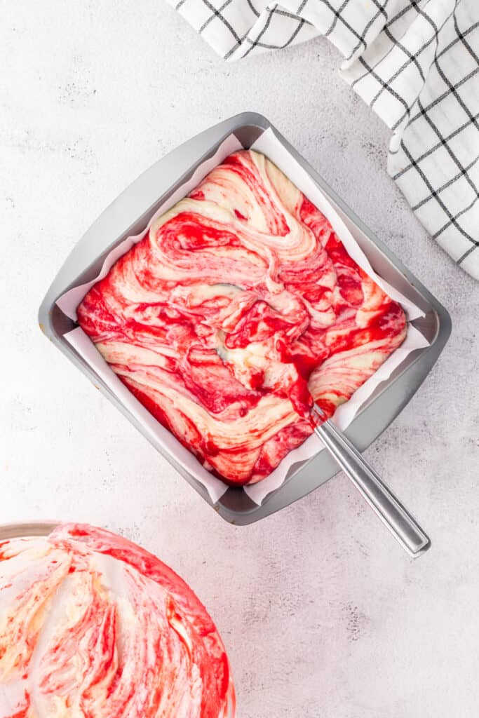 White chocolate raspberry fudge spread into parchment-lined pan with visible swirls