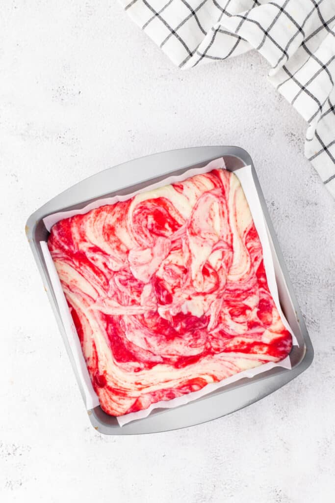 Overhead view of white chocolate raspberry fudge swirled with raspberry puree in a parchment-lined pan