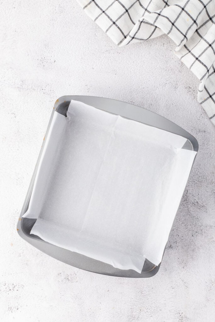 Square baking pan lined with parchment paper prepared for fudge