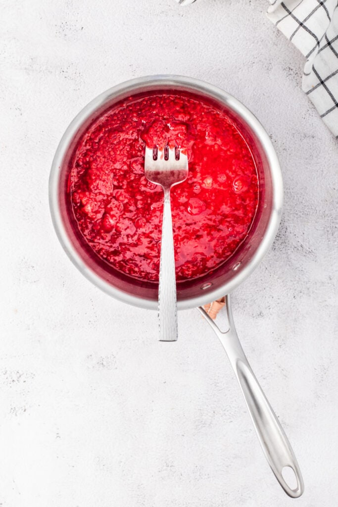 Cooked raspberry mixture thickening in a saucepan with a fork