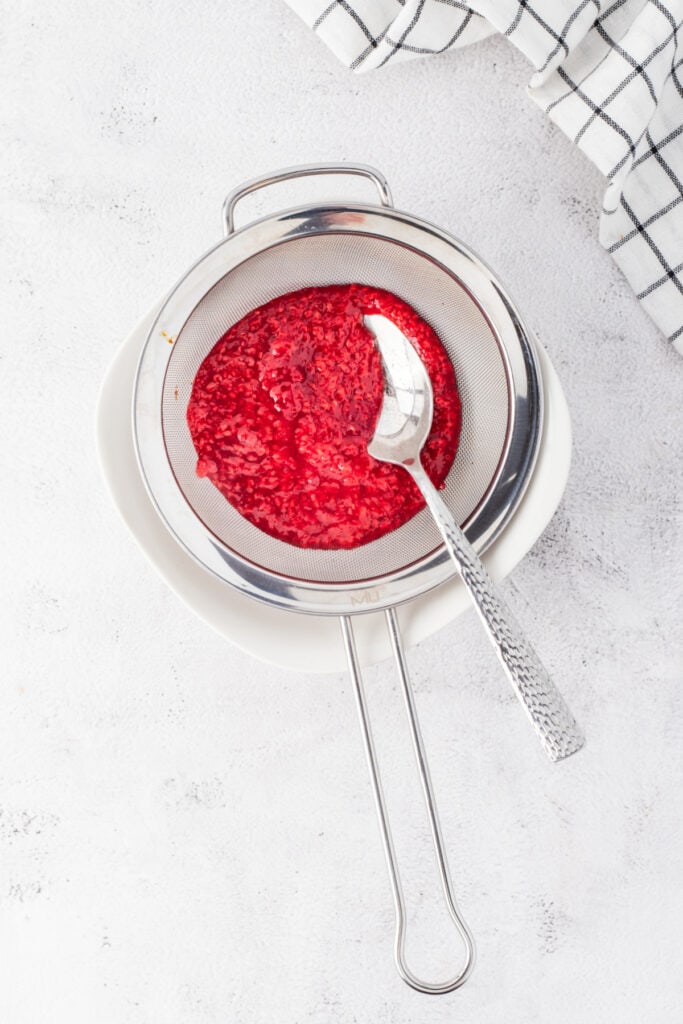 Raspberry puree being strained through a fine mesh strainer