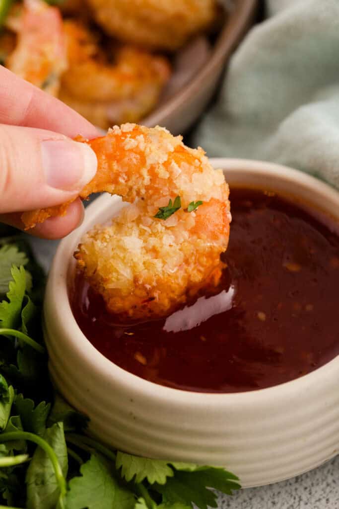 Hand dipping a crispy coconut shrimp into a bowl of sweet chili sauce.