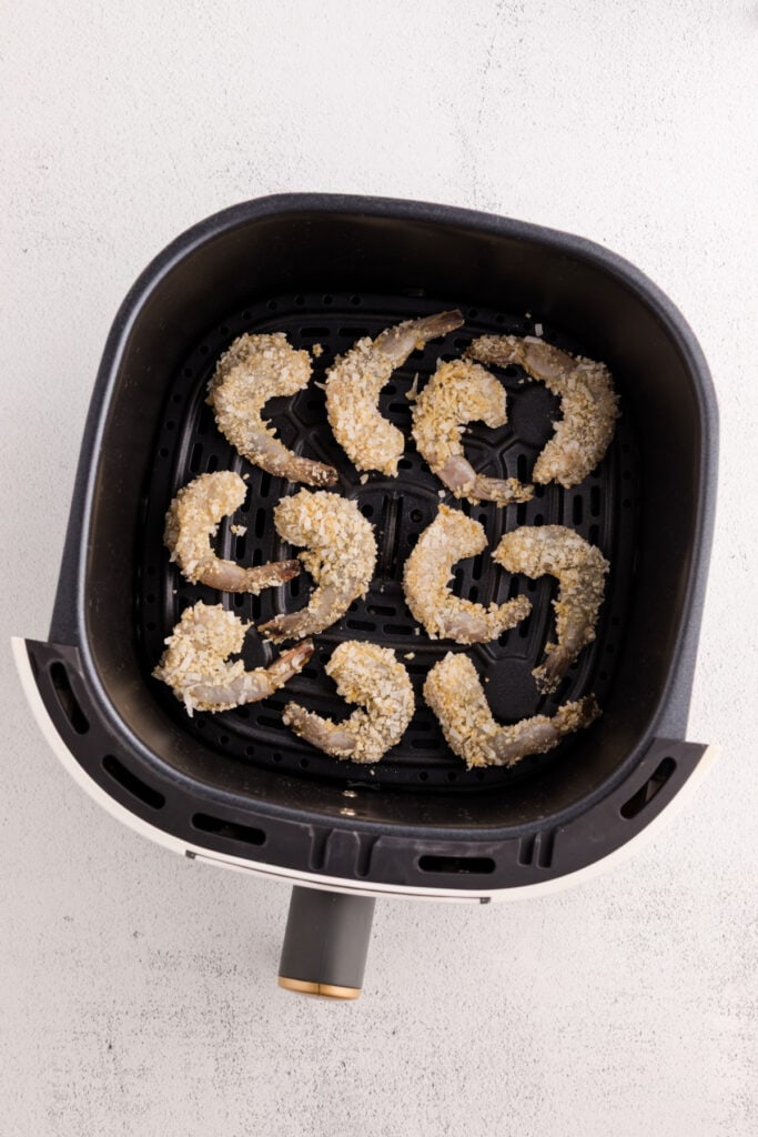 Breaded raw shrimp arranged in a single layer inside an air fryer basket.