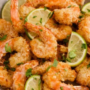 Close up of crispy coconut shrimp garnished with lime wedges and chopped cilantro.
