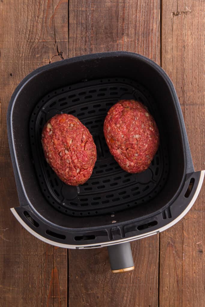 Two shaped raw meatloaves placed inside an air fryer basket.