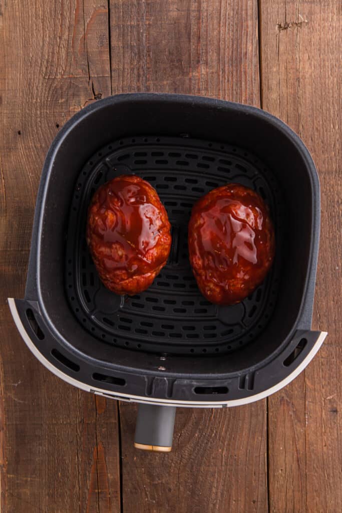 Two raw meatloaves in an air fryer basket topped with ketchup glaze.