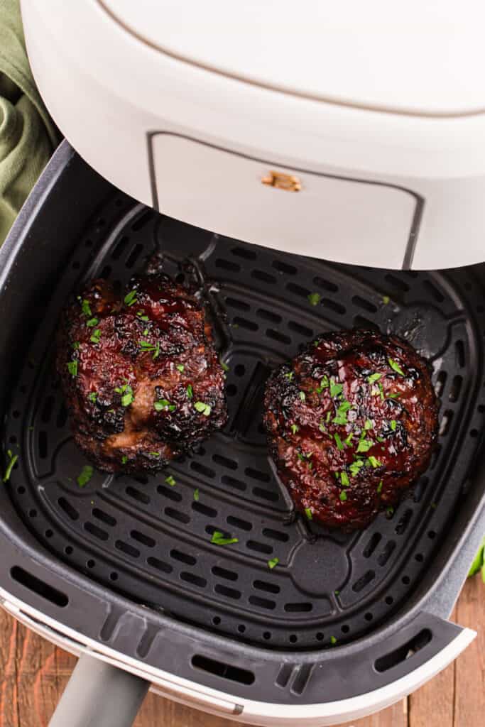 Two cooked glazed meatloaves inside an air fryer basket sprinkled with chopped parsley.