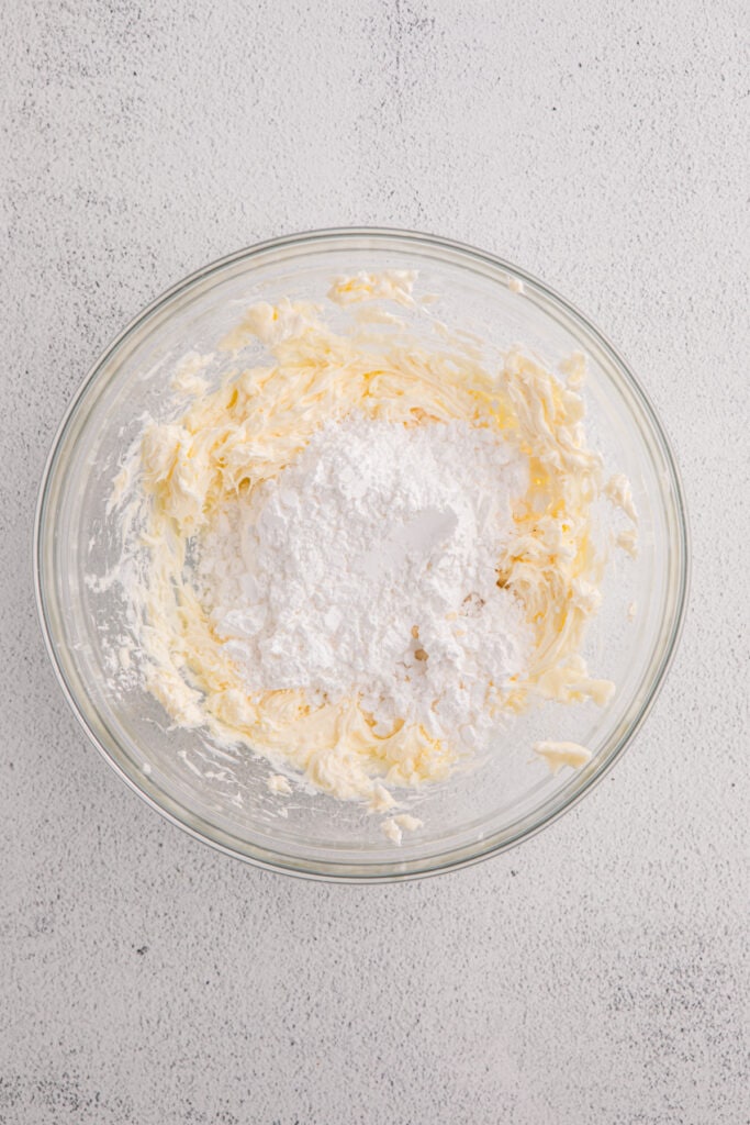 Glass bowl with cream cheese, butter, and powdered sugar before mixing