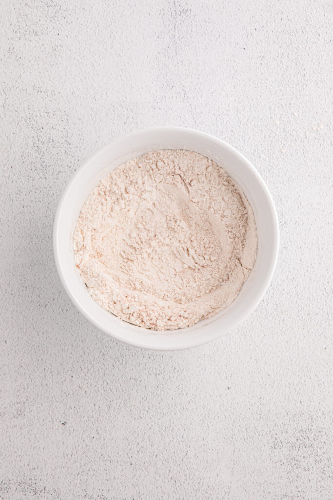 White bowl with dry ingredients whisked together on a light textured surface