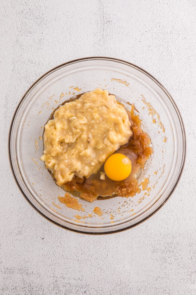 Glass bowl with mashed bananas, egg, brown sugar mixture, and oil before mixing