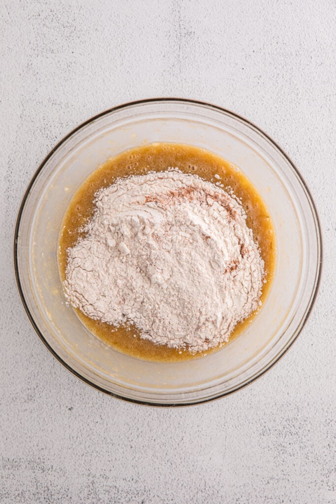 Glass bowl with wet ingredients topped with dry ingredient mixture before stirring