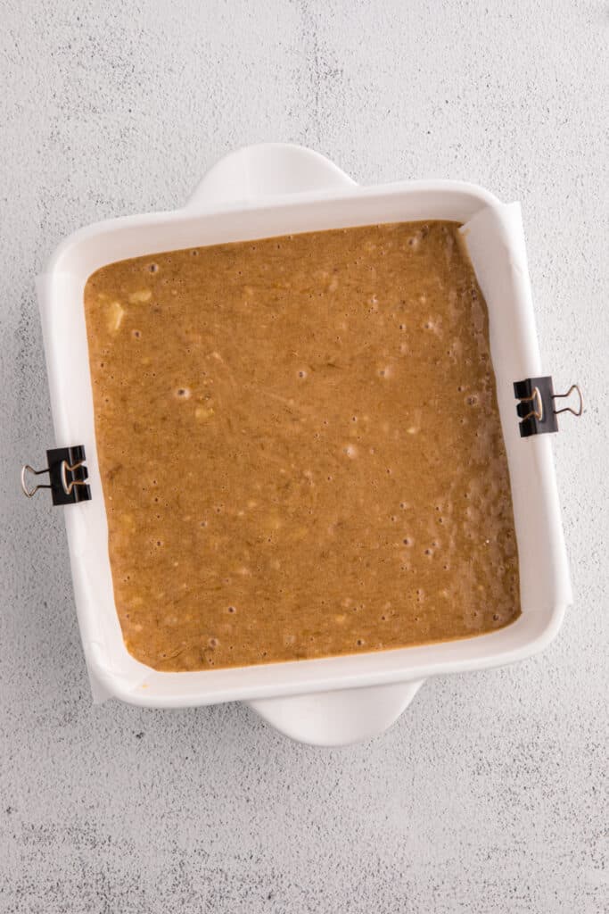 Square baking dish lined with parchment paper filled with banana brownie batter