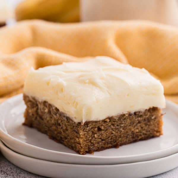 Frosted banana brownies cut into squares on a wooden board with a banana and coffee mug in the background
