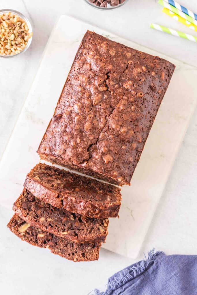Whole brownie banana bread loaf on a white cutting board with several slices cut in front.