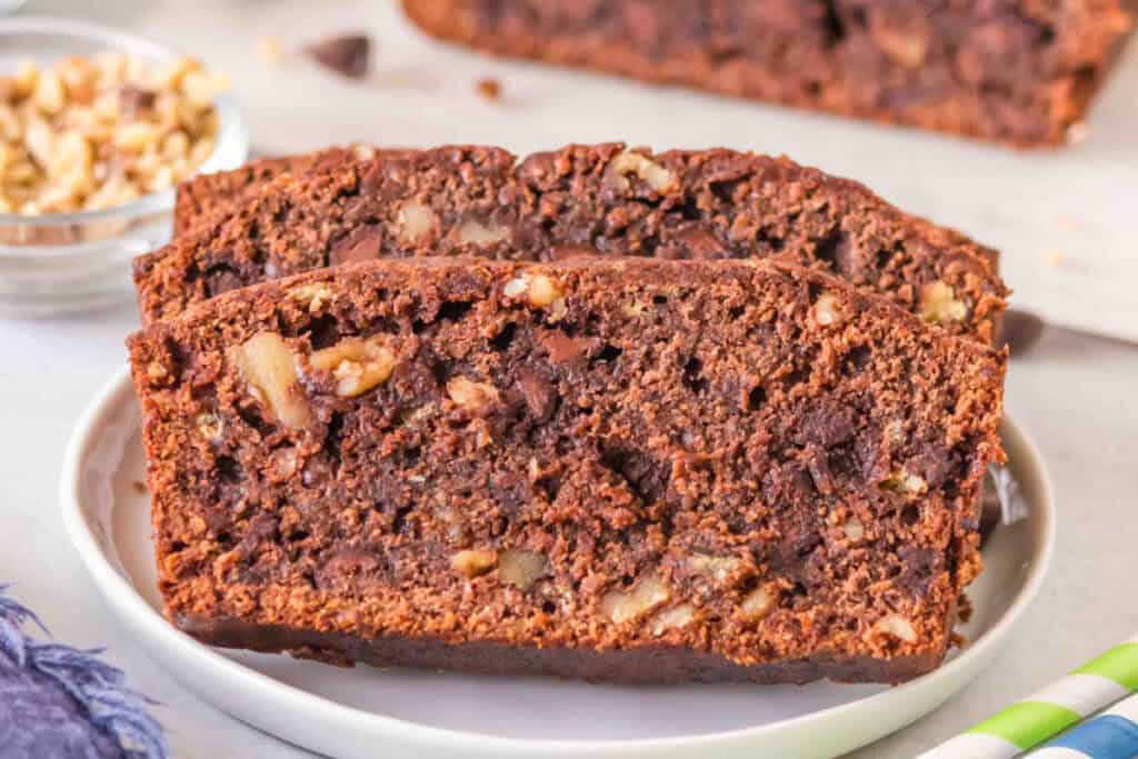 Two slices of brownie banana bread on a white plate with chocolate chips and walnuts visible.